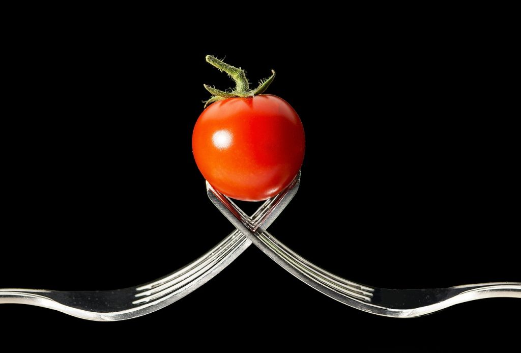 Spaghetti - Bild von zwei geflochtenen Gabeln, die eine Tomate halten