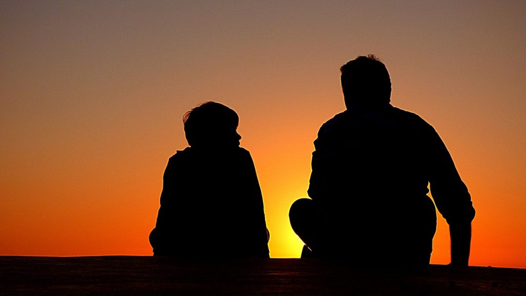 Dad - An orange sky at sunset on which stand the silhouettes of a father with his own child