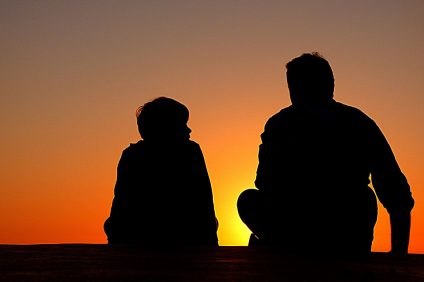 Dad - An orange sky at sunset on which stand the silhouettes of a father with his own child