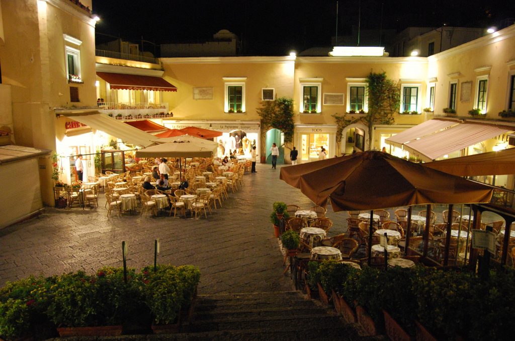 Capri. La piazzetta di sera con gli eleganti tavolini dei bar all'aperto riparati dai tendaggi