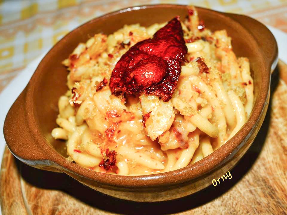 Pici with chickpea flour, cod and cruschi peppers in a terracotta dish