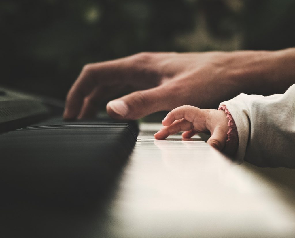 Piero Angela. Tastiera di pianoforte su cui delicatamente si poggia la mano di un adulto e quella di un bambino