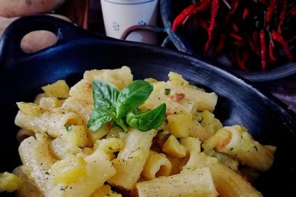 pot with bacon rigatoni and basil leaves
