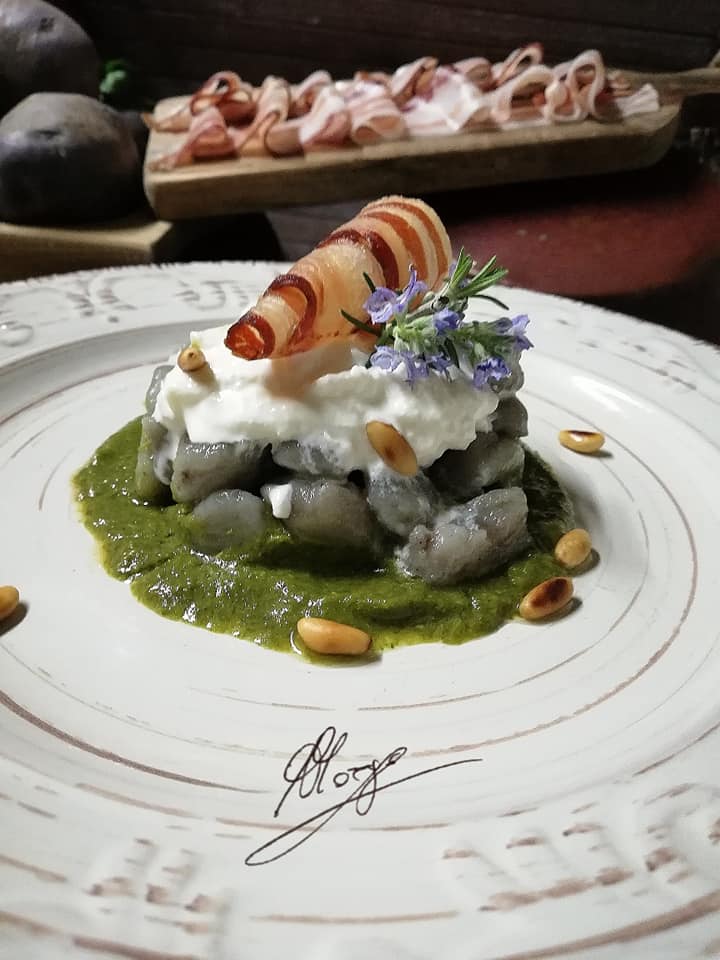 Gnocchi di patate viola con burrata bacon croccante e crema di cime di rapa in piatto