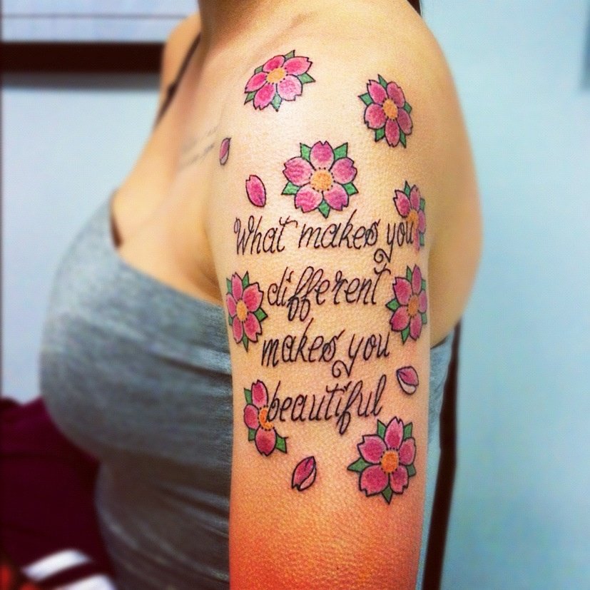 tatuaggio femminile su braccio con fiori rosa e una frase 