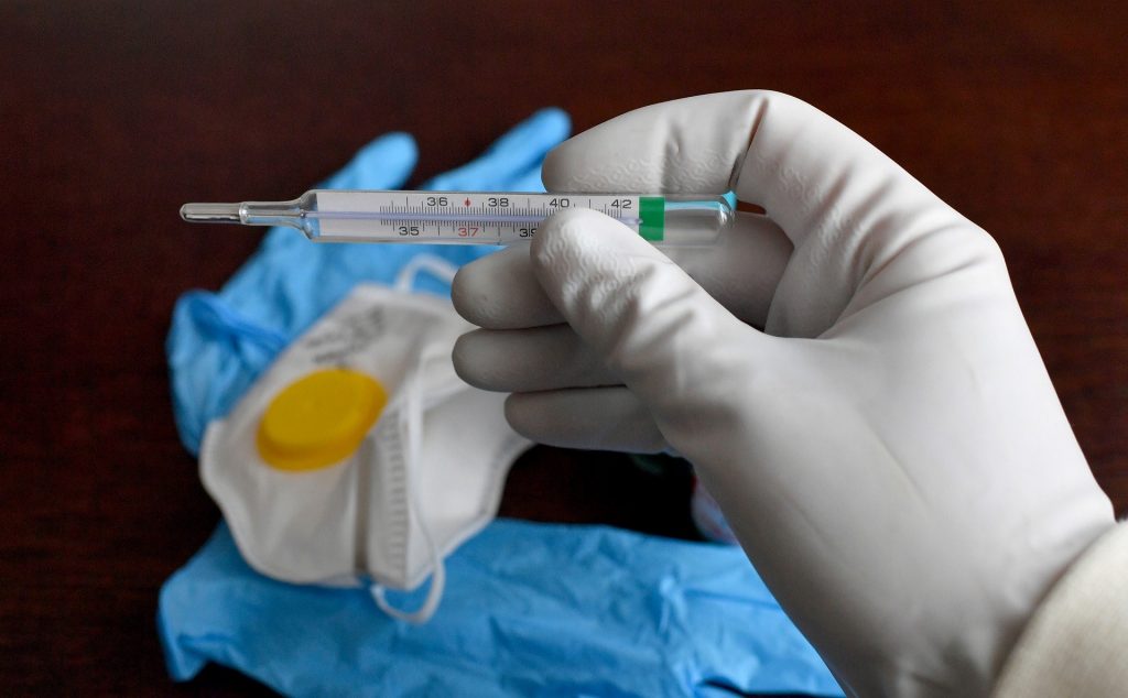 coronavirus - gloved hands holding a thermometer