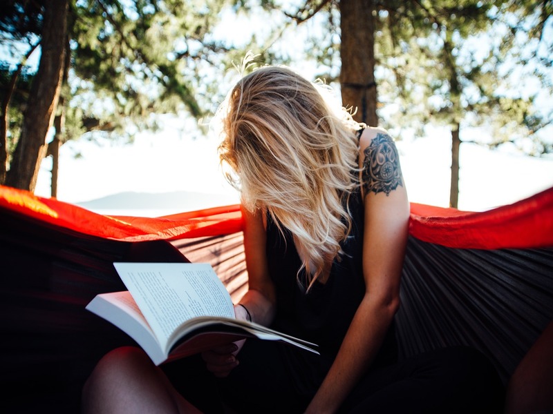 Girl in a meadow reads a book in solitude and inertia