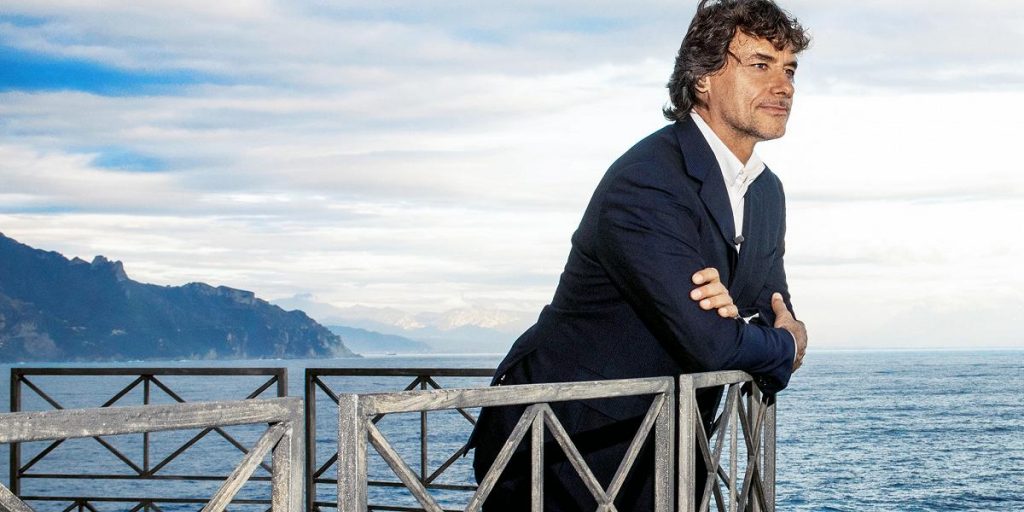 alberto angela leans out from the balustrade with the sea in the background