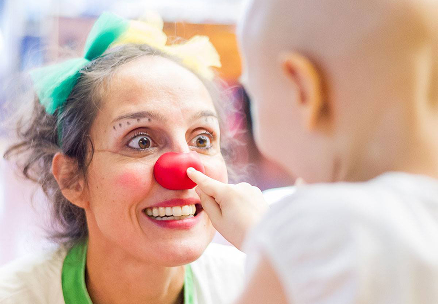 children - child touching the red nose of a doctor dressed as a clown