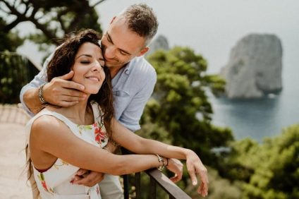 luna di miele in Italia - Coppia si abbraccia con lo sfondo dei faraglioni di Capri