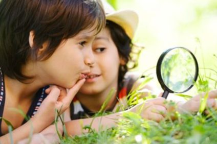 L'immagine rappresenta due bambini che stanno cercando nell'erba gli insetti da studiare