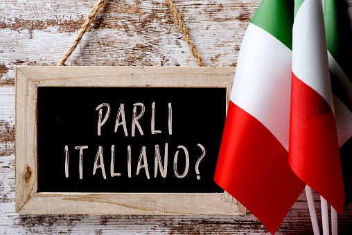Iscriviti ai nostri corsi di italiano! Lavagna con su scritto: "Parli italiano?" e bandiere dell'Italia. Fonte foto: Pixabay. 