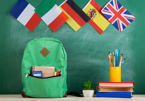 Iscriviti ai nostri corsi di italiano! Zaino, libri e bandiere europee sullo sfondo. Fonte foto: Pixabay. 