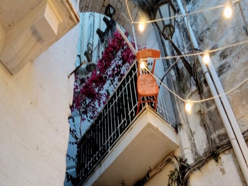 Un balcone pieno di fiori a Ostuni con appesa una sedia ornamentale