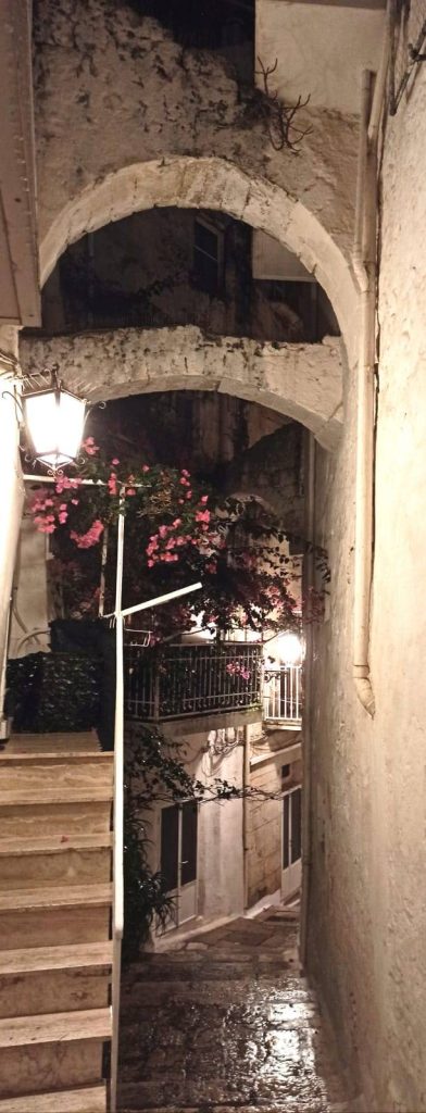 Un vicolo bianco a Ostuni e balconi con fiori 